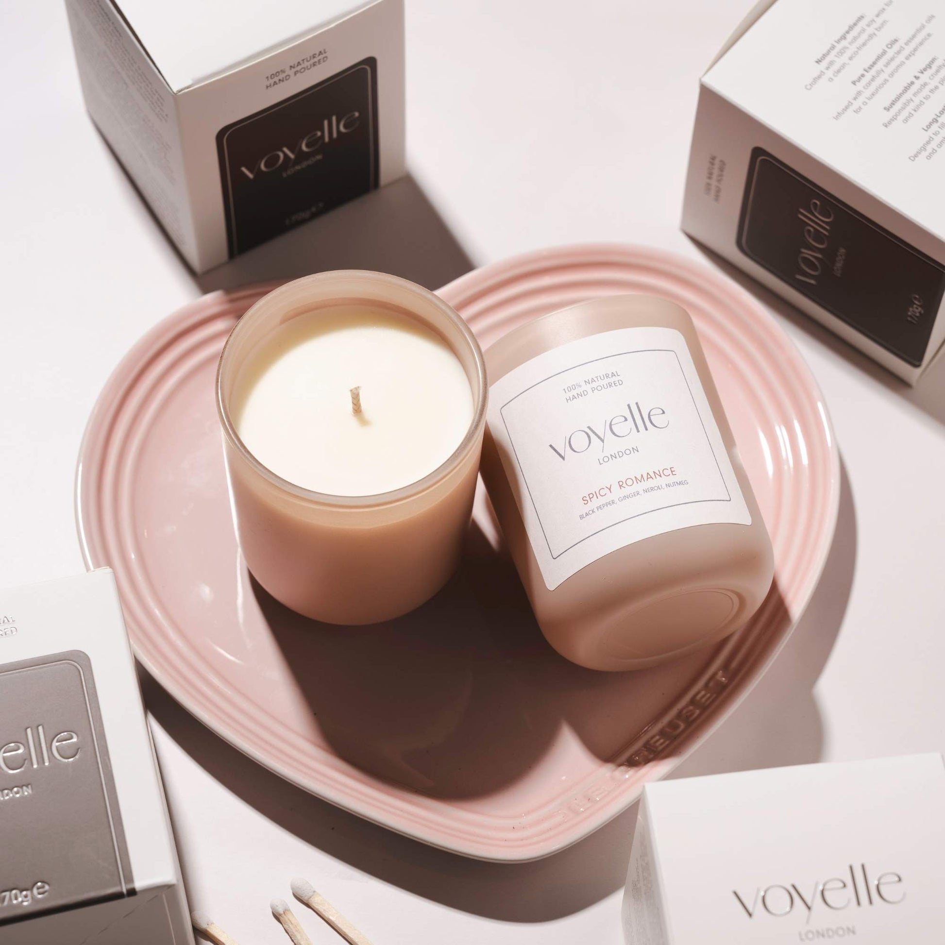 Two Voyelle Spicy Romance candles on a pink heart-shaped plate, surrounded by branded packaging