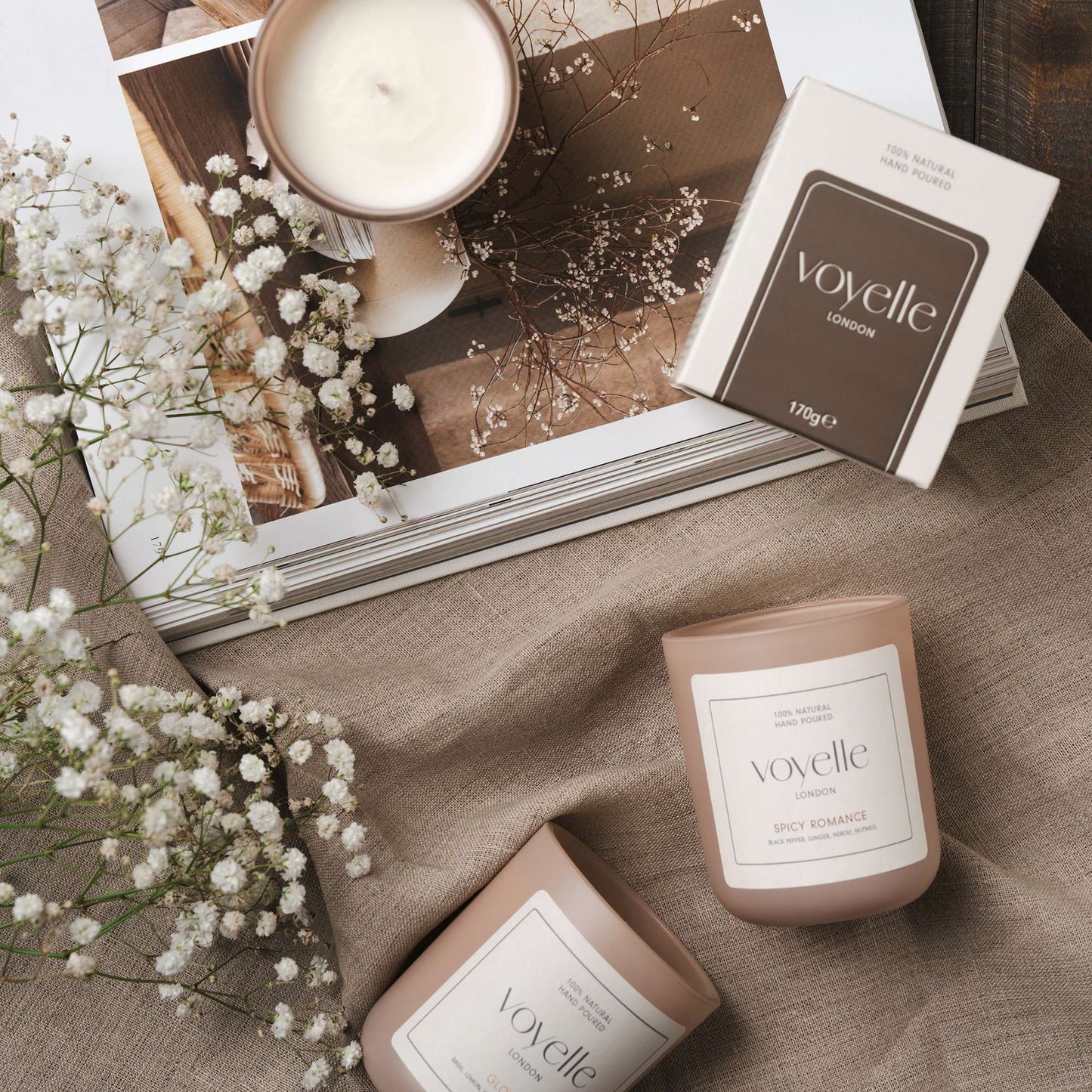 Voyelle candles on linen fabric with baby's breath flowers and an open magazine