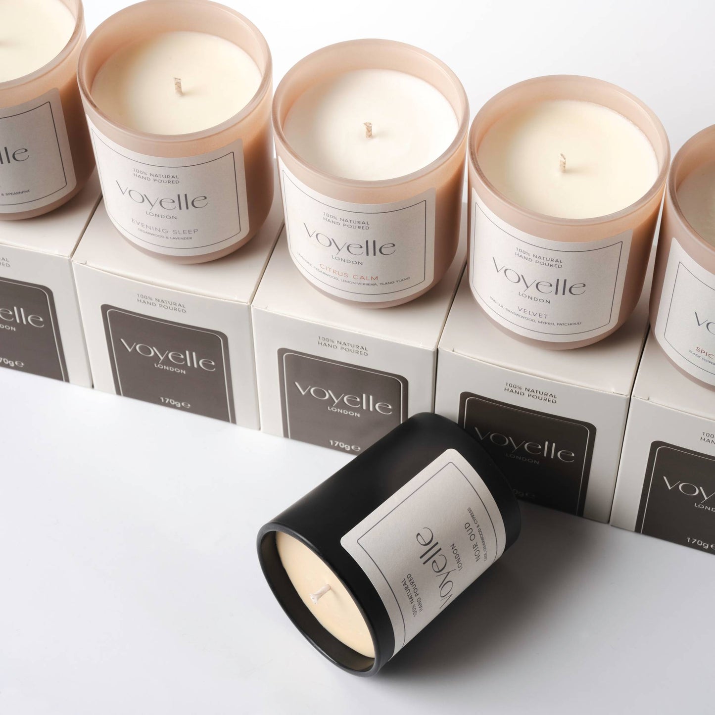 Assorted Voyelle candles displayed in a row with Noir Oud candle lying in front