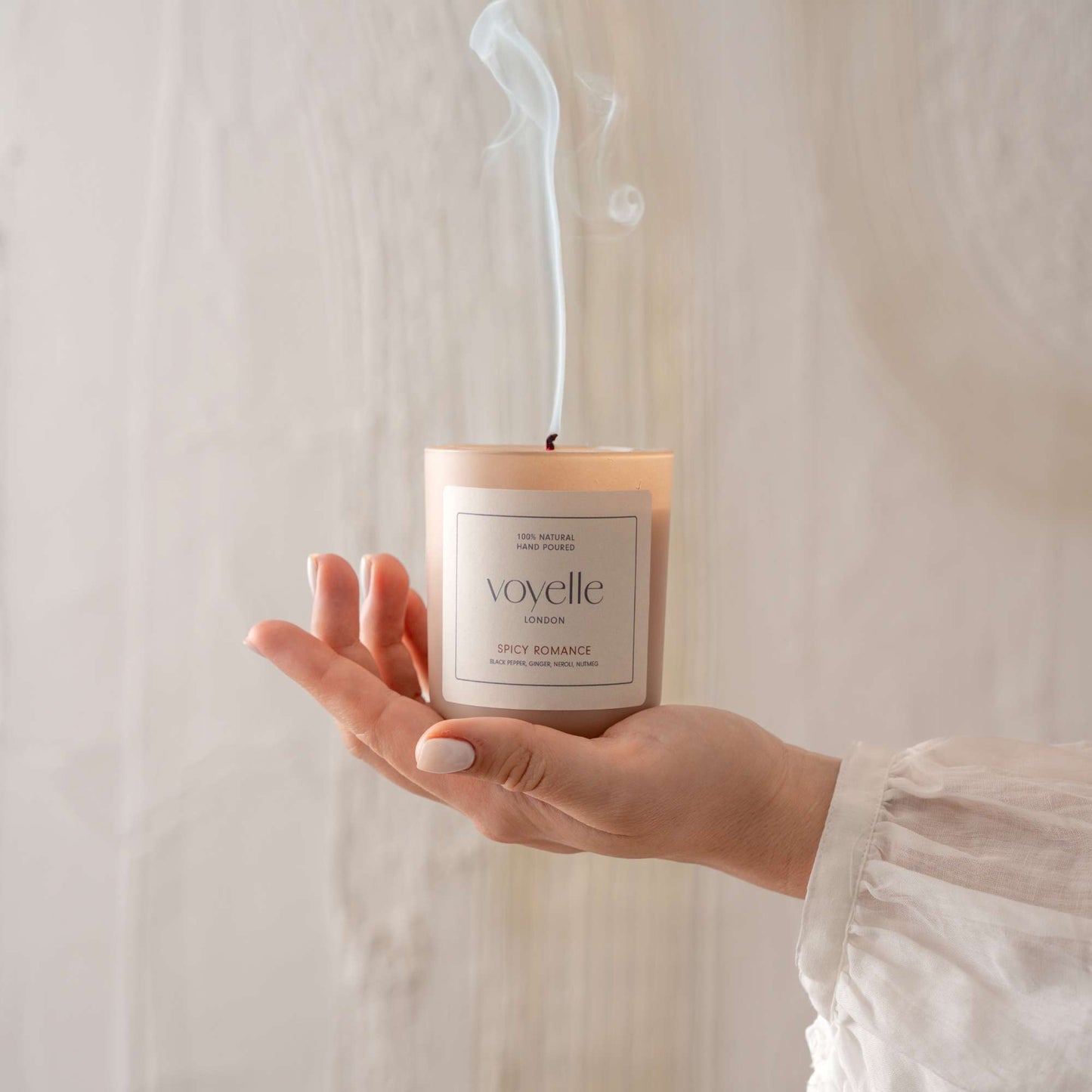 A hand holding a Voyelle candle with smoke rising after extinguishing the flame