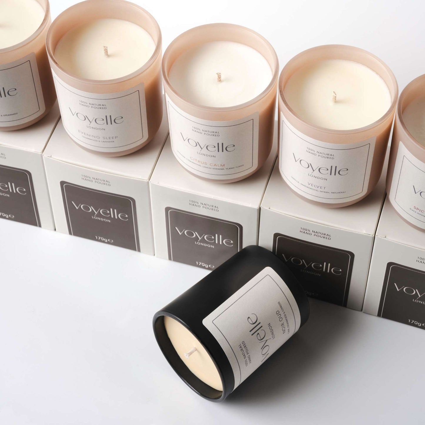 Collection of Voyelle scented candles in glass jars and packaging boxes, arranged neatly on a white background
