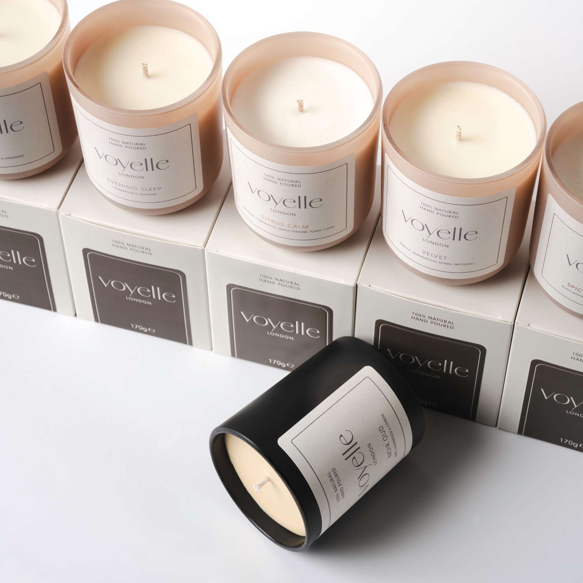 Collection of Voyelle scented candles in glass jars and packaging boxes, arranged neatly on a white background