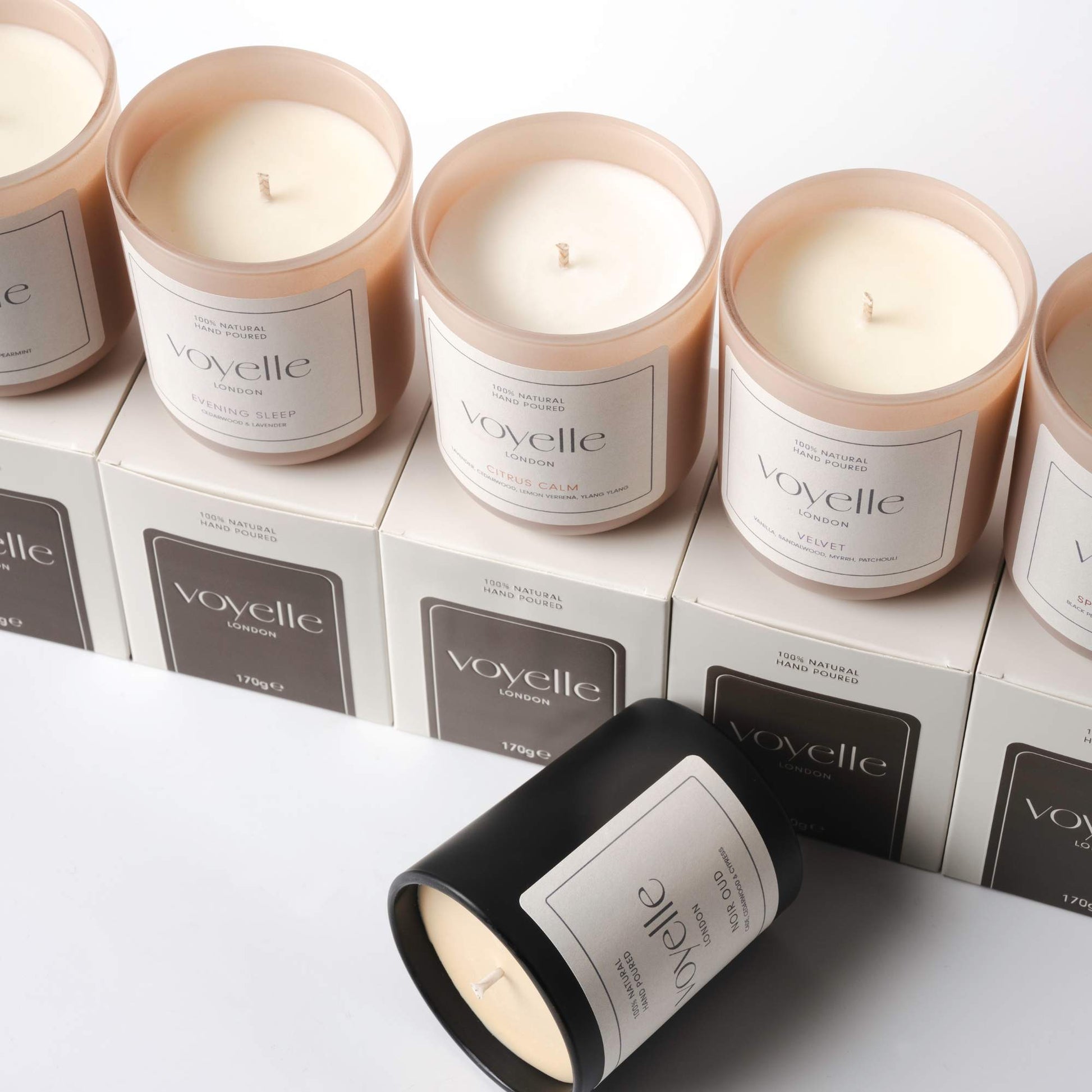 Voyelle scented candles arranged on branded boxes, featuring fragrances like Evening Sleep, Citrus Calm, Violet, and Noir Oud