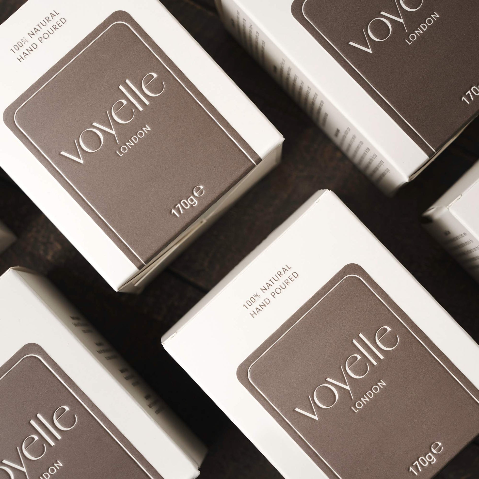 Voyelle London 170g candle boxes arranged in a flat lay on dark wood surface