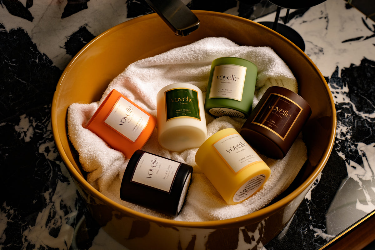 The Voyelle candle collection — six scents arranged in an amber basin on marble