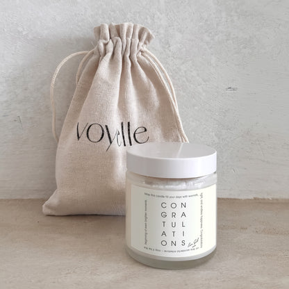 Jar of 'Congratulations' with a beige drawstring bag labeled 'Voyelle' on a light wooden surface.