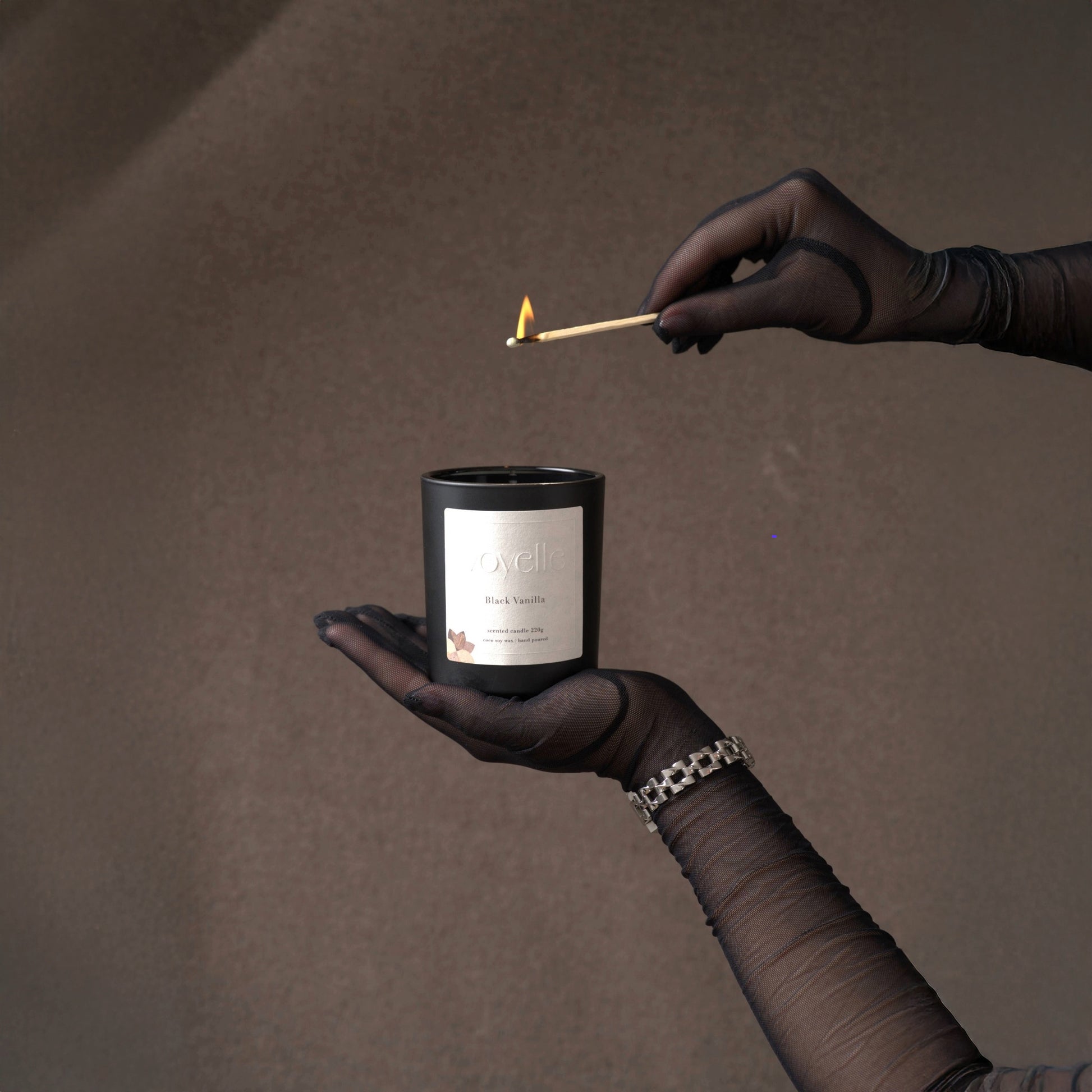 Luxurious Black Vanilla soy candle by Voyelle being lit – elegant hand-poured candle in black jar