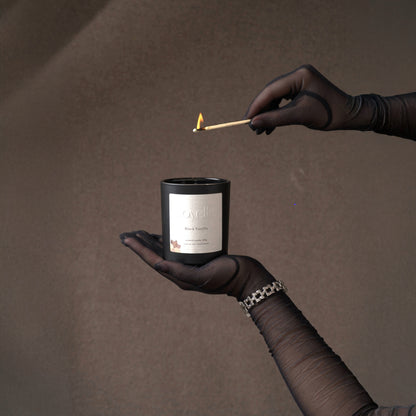 Luxurious Black Vanilla soy candle by Voyelle being lit – elegant hand-poured candle in black jar