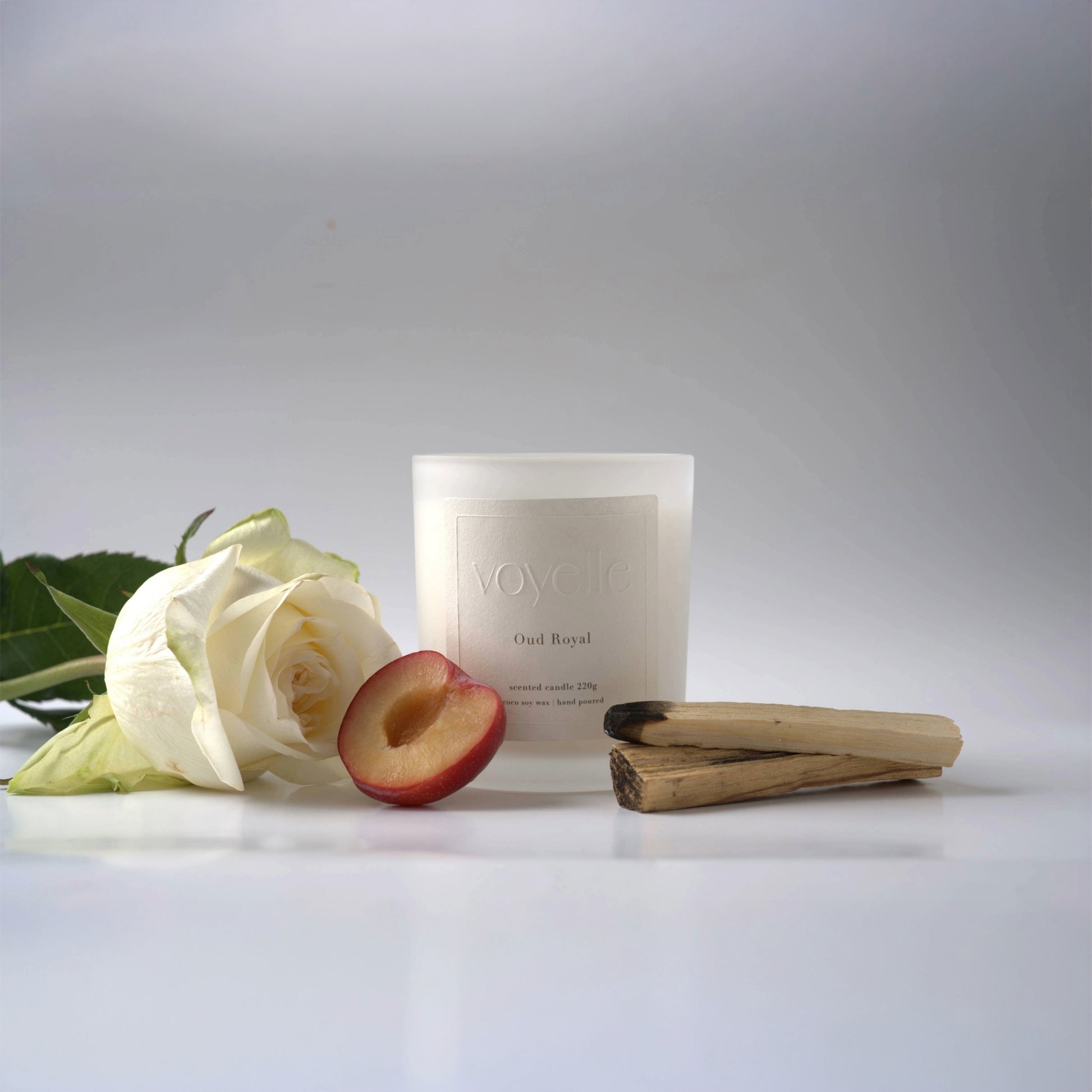 Voyelle Oud Royal candle with white rose, plum, and palo santo wood on white background