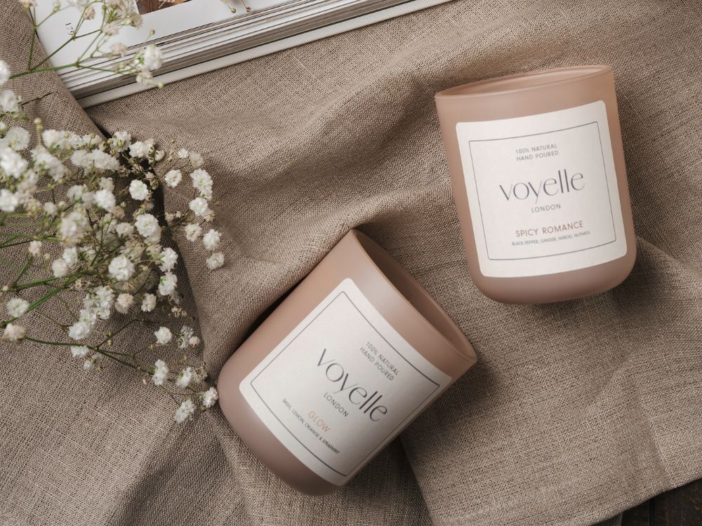 Voyelle handmade scented candles "Glow" and "Spicy Romance" on beige linen fabric with baby's breath flowers – luxury soy wax candles