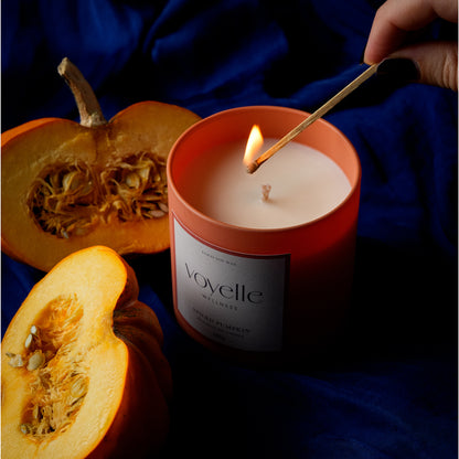 Lighting a Spiced Pumpkin candle with a long match beside cut pumpkin halves