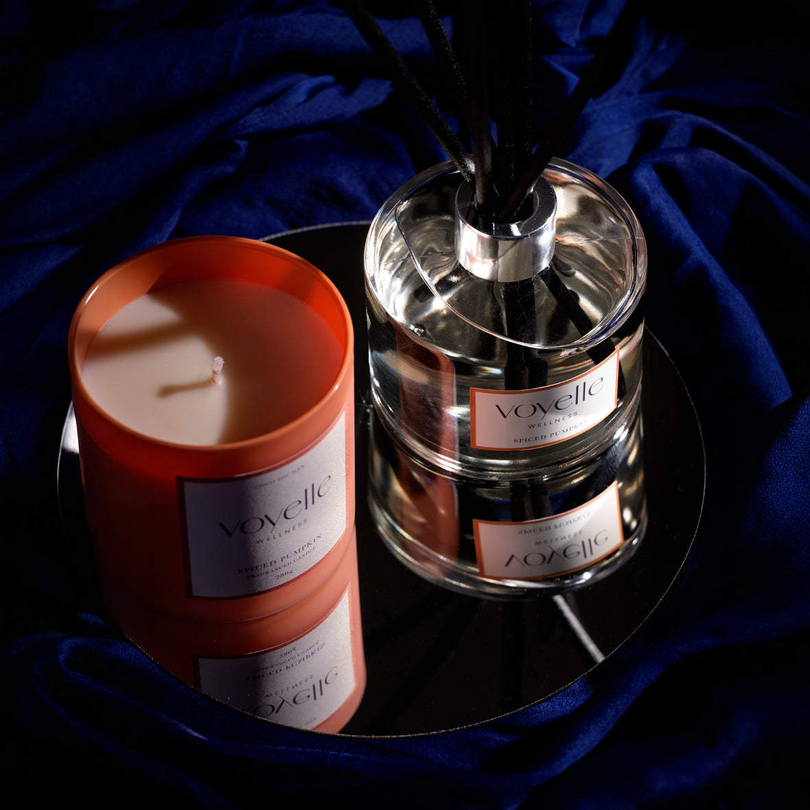 Spiced Pumpkin candle and matching reed diffuser on a round mirror over navy silk