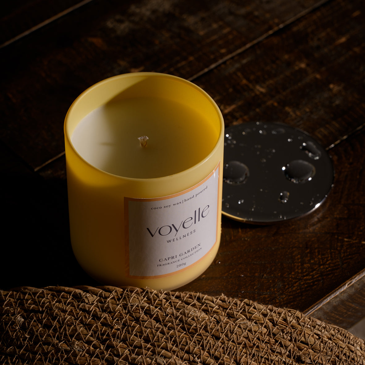 Capri Garden open candle on dark wood, chrome lid with raindrops beside